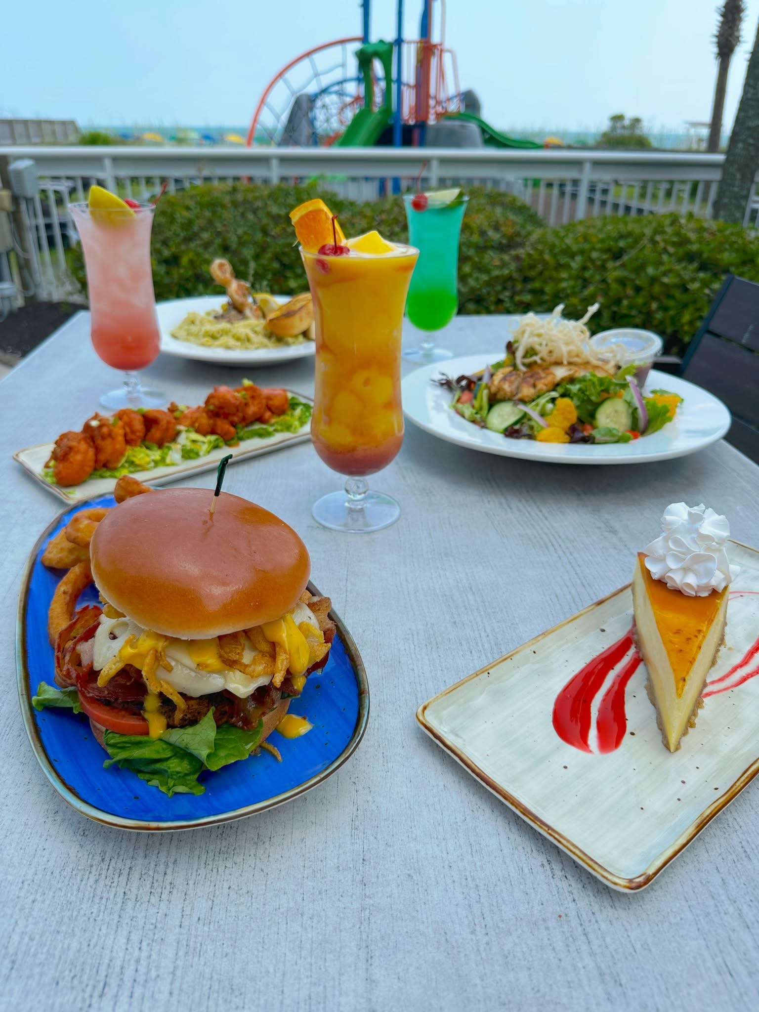A table with various dishes and drinks, including a burger, salad, and cheesecake.